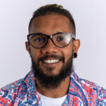 happy african american young man in colorful shirt wearing glasses looking at camera smiling cheerfully standing over white background