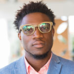 Serious trendy guy posing indoors. Closeup of young African American man wearing stylish glasses, bright shirt and jacket, looking at camera. Fashion or male portrait concept